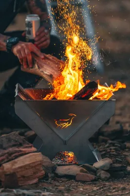 Hands feeding a campfire in a steel fire pit