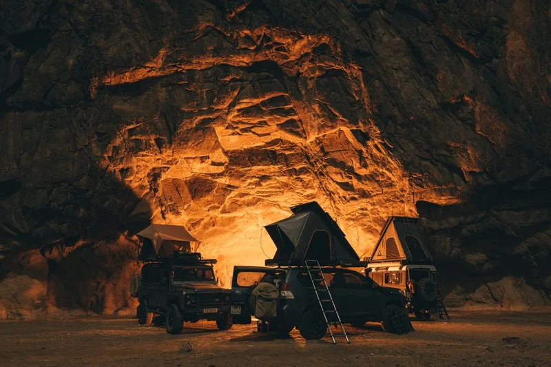 Three vehicles with rooftop tents camped inside a glowing rock cave
