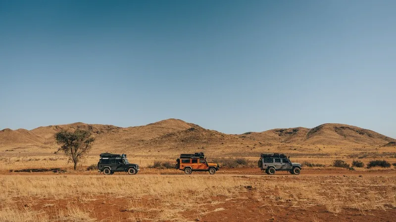 Three Land Rover Defenders parked in dry grassland